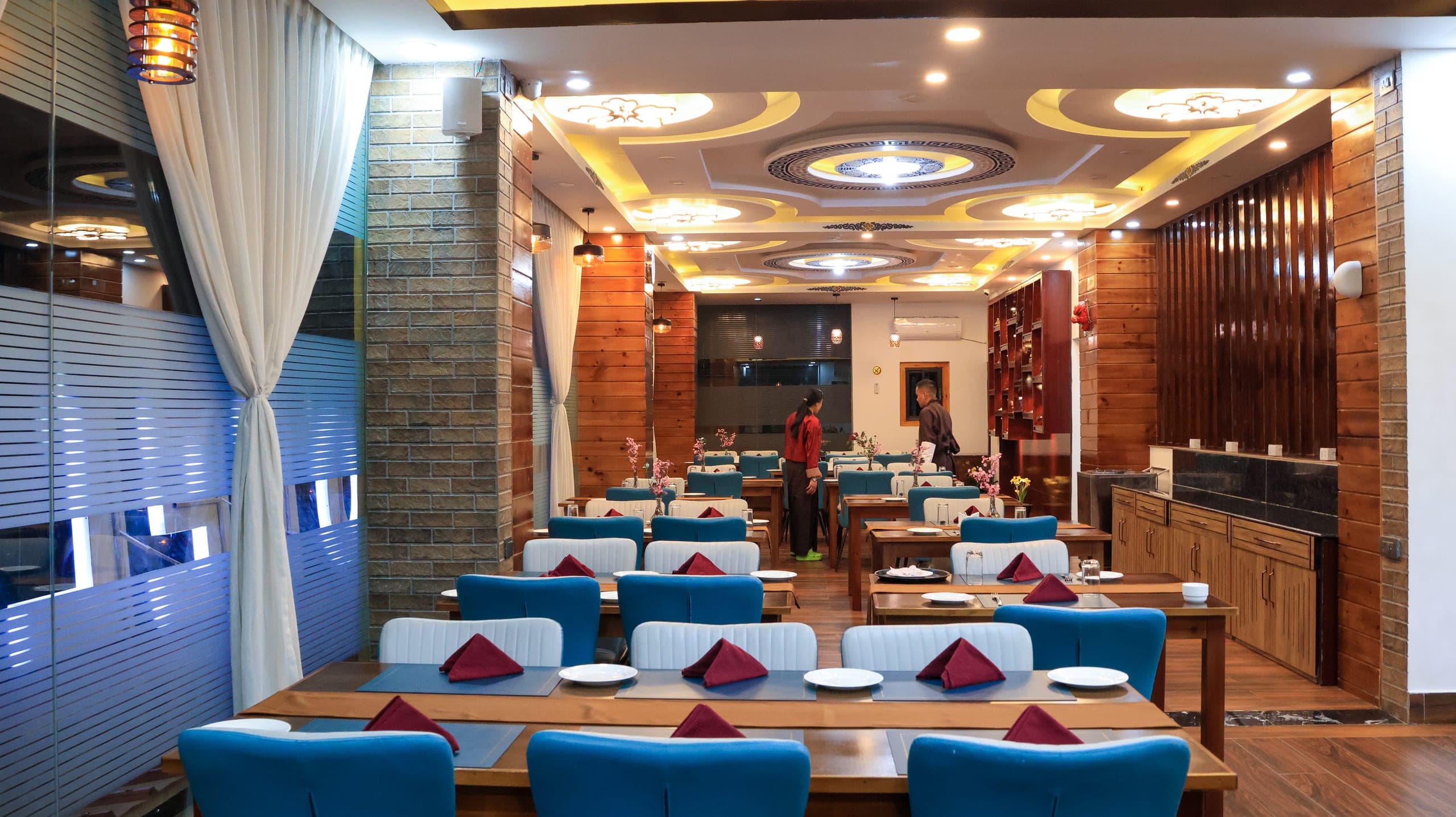 Dining room with blue chairs, patterned ceiling lights and a wood-panelled wall