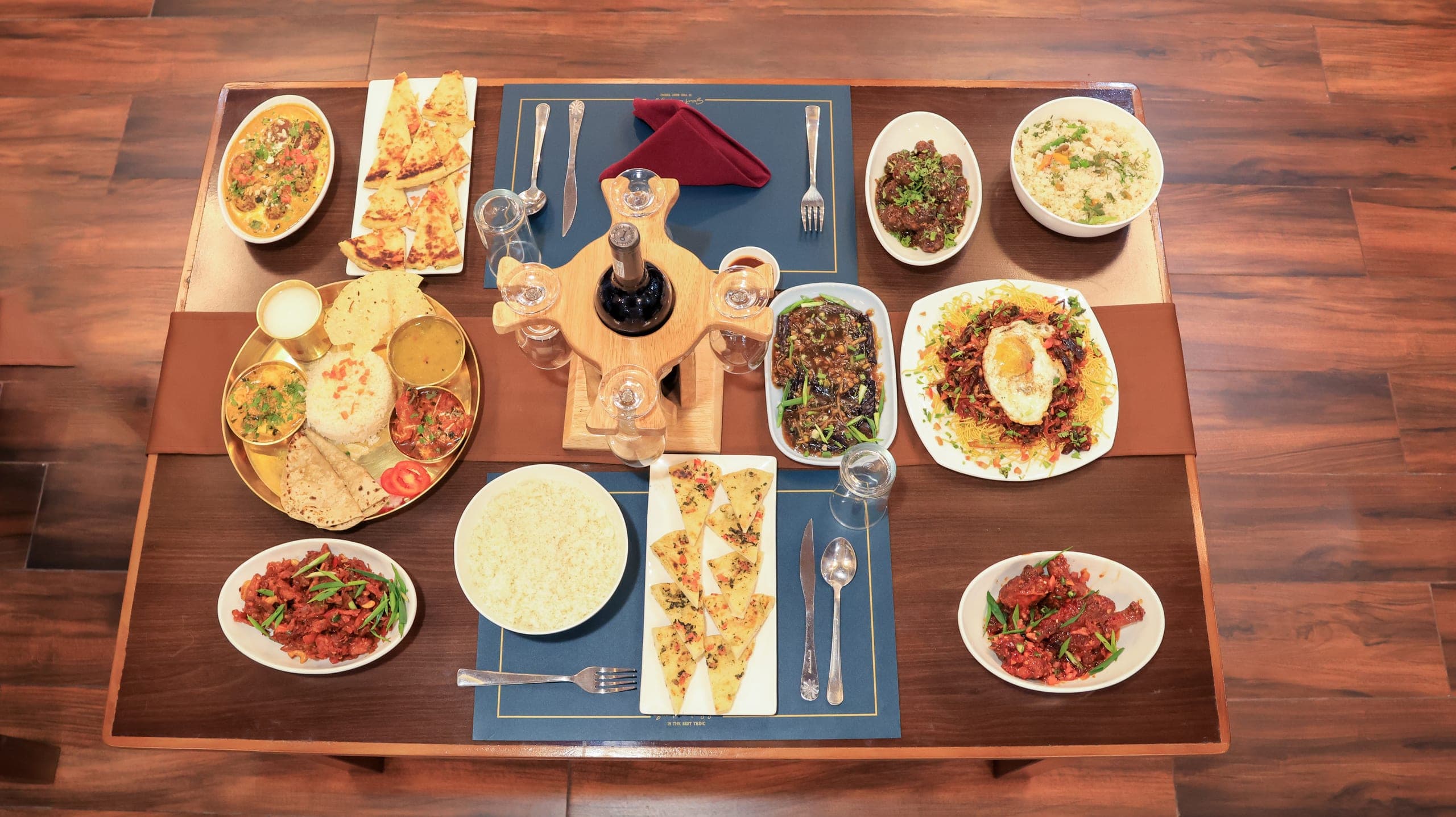 A table spread of rice, curries, noodles, flatbreads and stir-fries seen from above