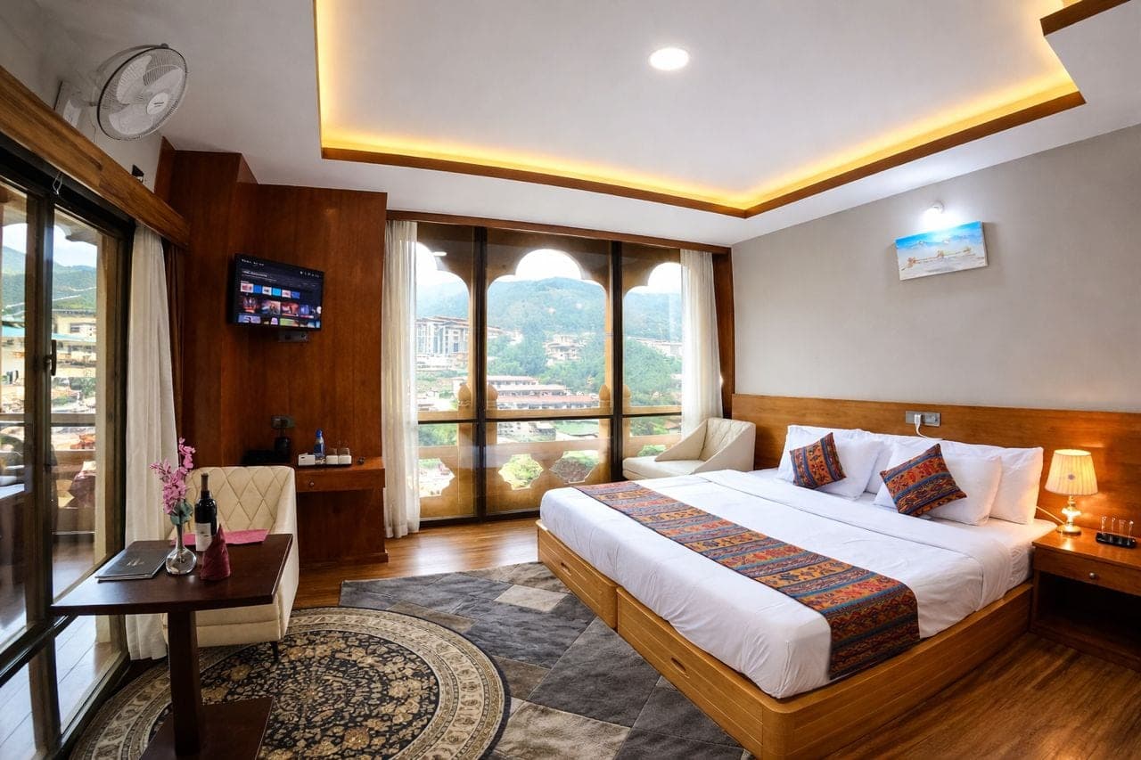 Double Deluxe room with a large bed, Bhutanese textile runner and arched windows onto the mountains